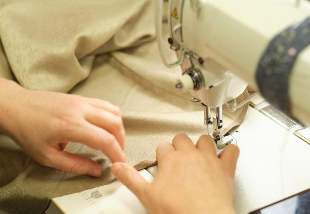 Close up view of sewing process. Female hands stitching fabric on professional manufacturing machine at workplace. 
