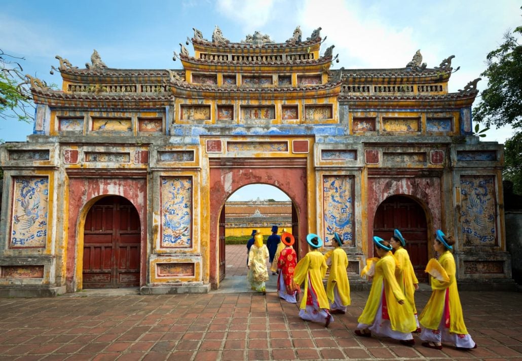 People in traditional costumes walk under an archway in the Imperial City of Hue, Vietnam.