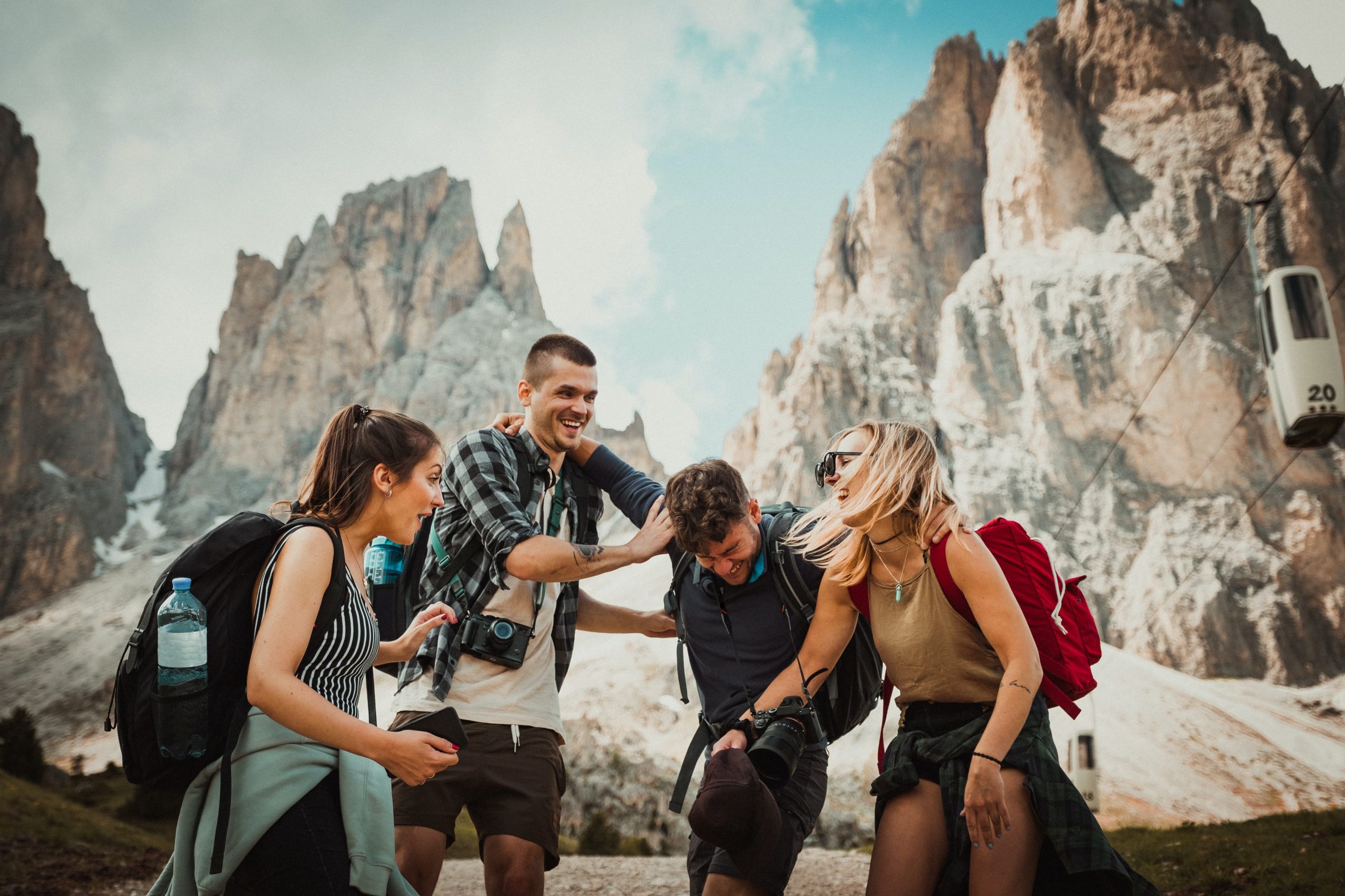 A group of four friends, two girls and two guys, laughing together during an outdoor hike surrounded by mountains.