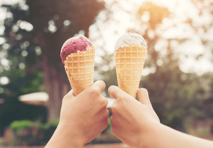 Woman’s hands holding melting ice cream waffle cone in hands-on light summer nature background.