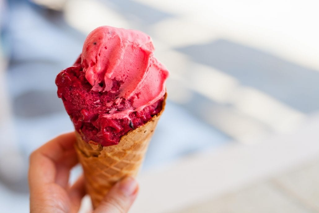 Close up woman's hand holding fresh waffle cone with raspberry ice cream