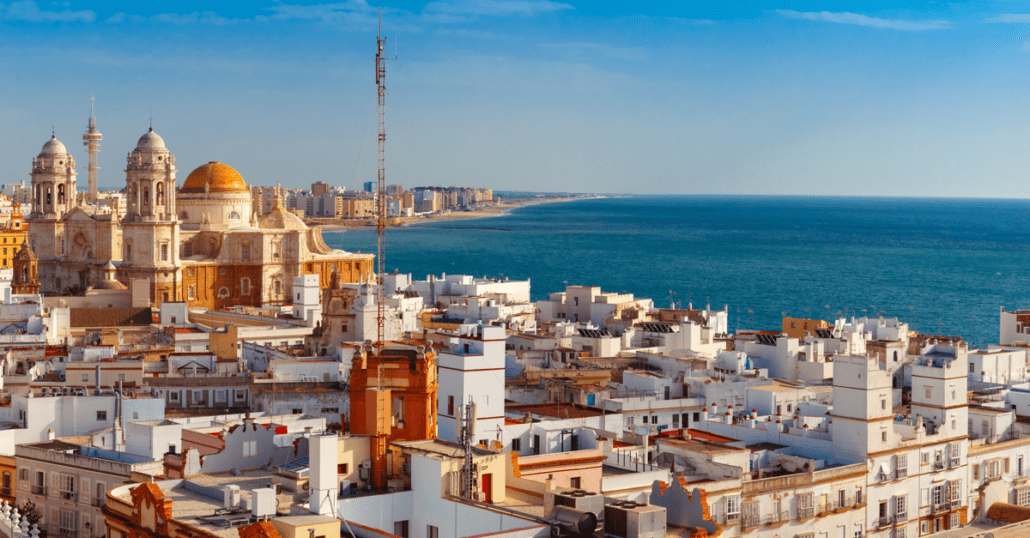 View of the historic white and orange buildings by the blue ocean in Cadiz, Spain.