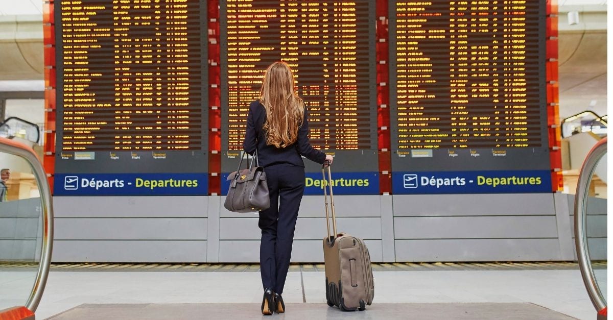 Woman checking the departures table on the airport with her carry on luggage on hand.