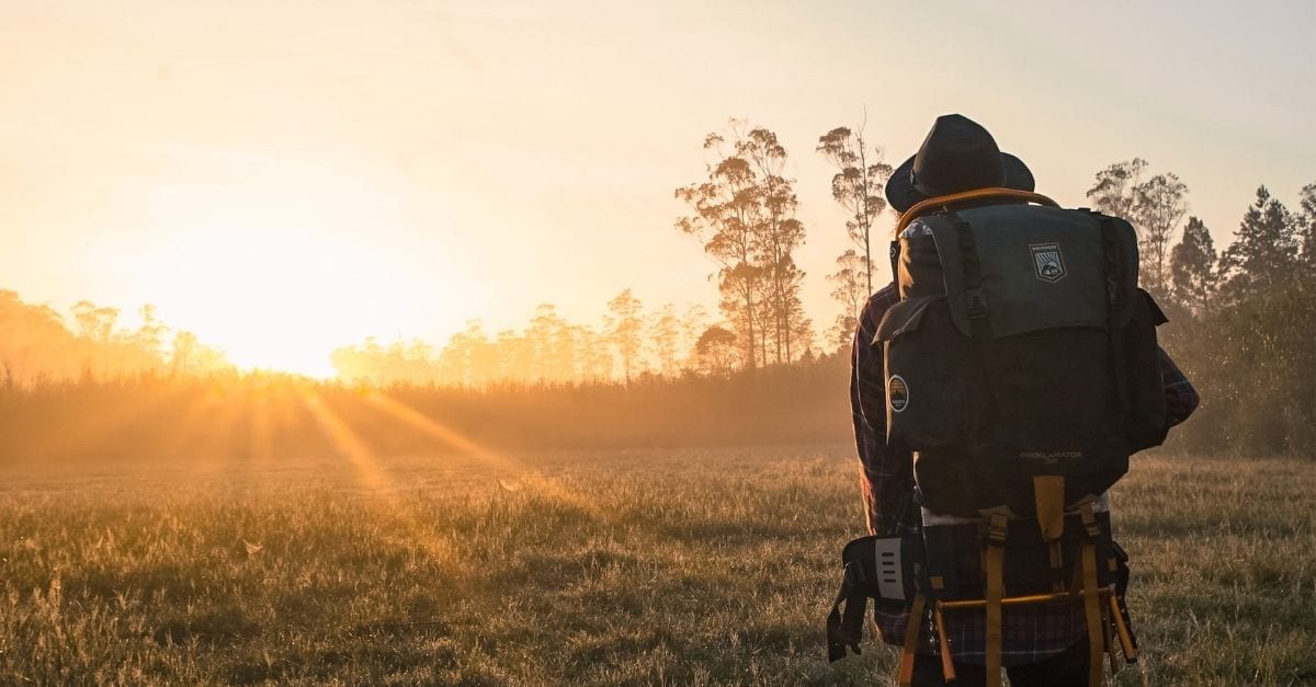 A backpacker watching the sunset on an extensive field filled with trees.