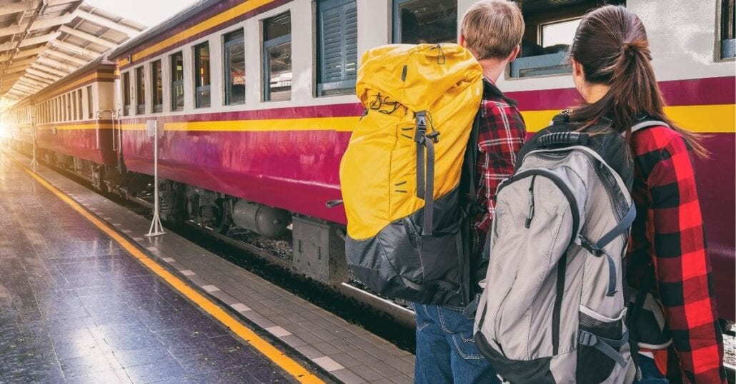 Two backpackers, a boy, and a girl, waiting for a train on the platform.