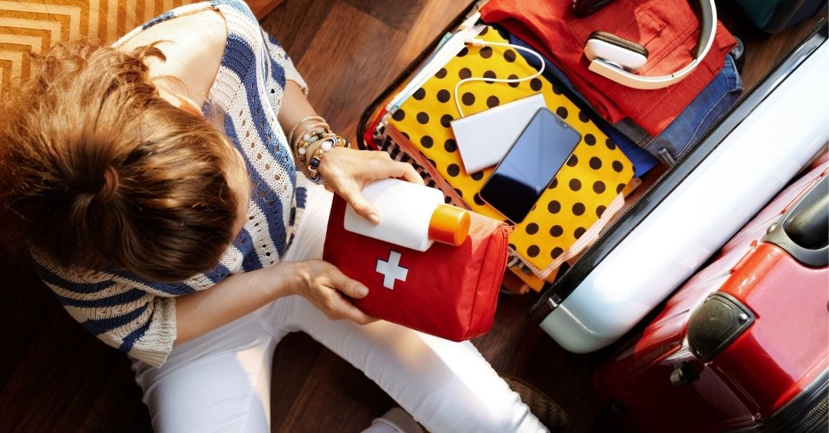 Top view of a young woman packing a first aid kit into her travel luggage.