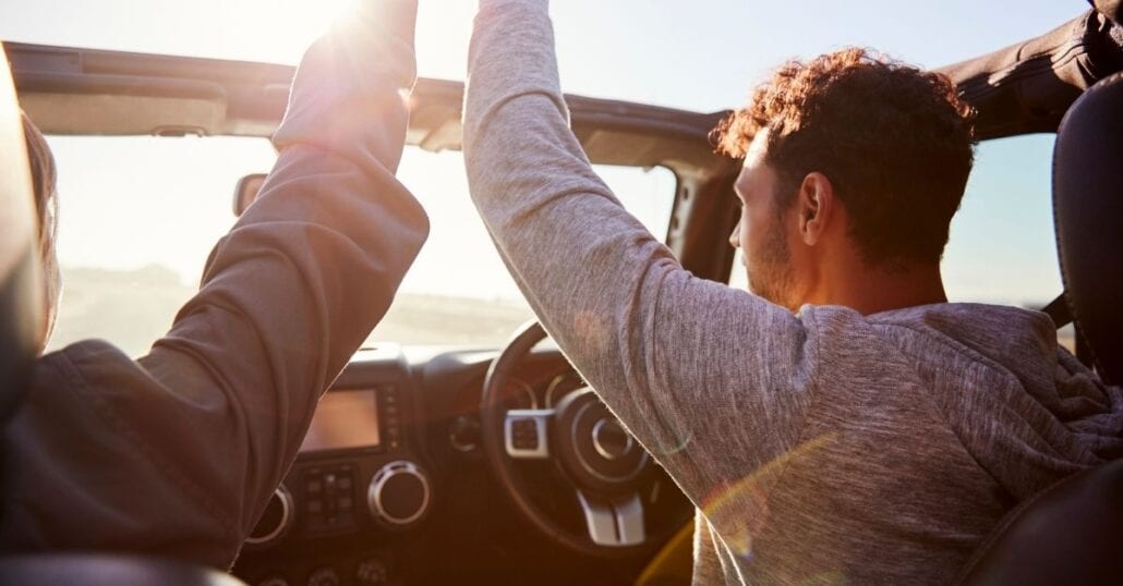 Two friends on a conversible car during a road trip.