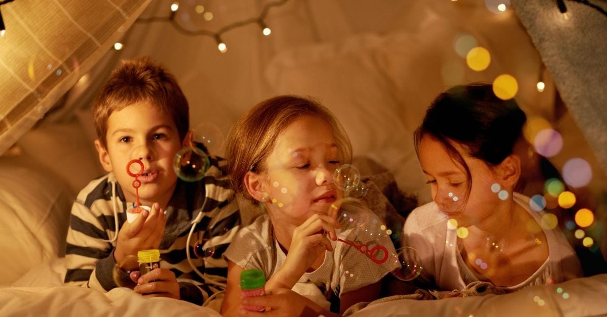 Three kids, a boy and two girls, playing at night inside a bedroom tent. 