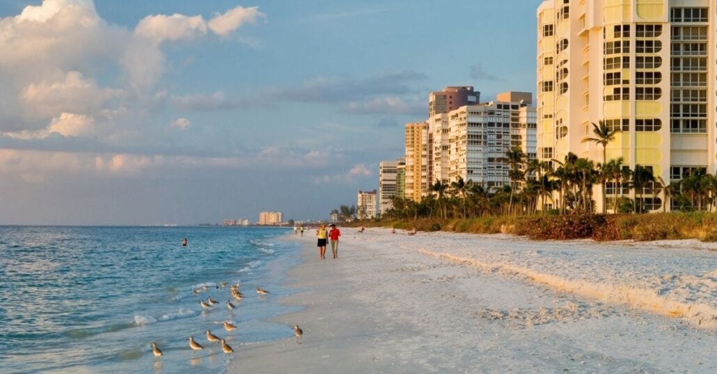 Two people walking by the ocean on a sandy beach in Naples, Florida.