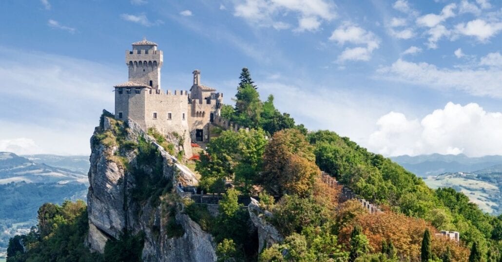 gezicht op de Drie Torens van San Marino boven een groene beboste heuvel.