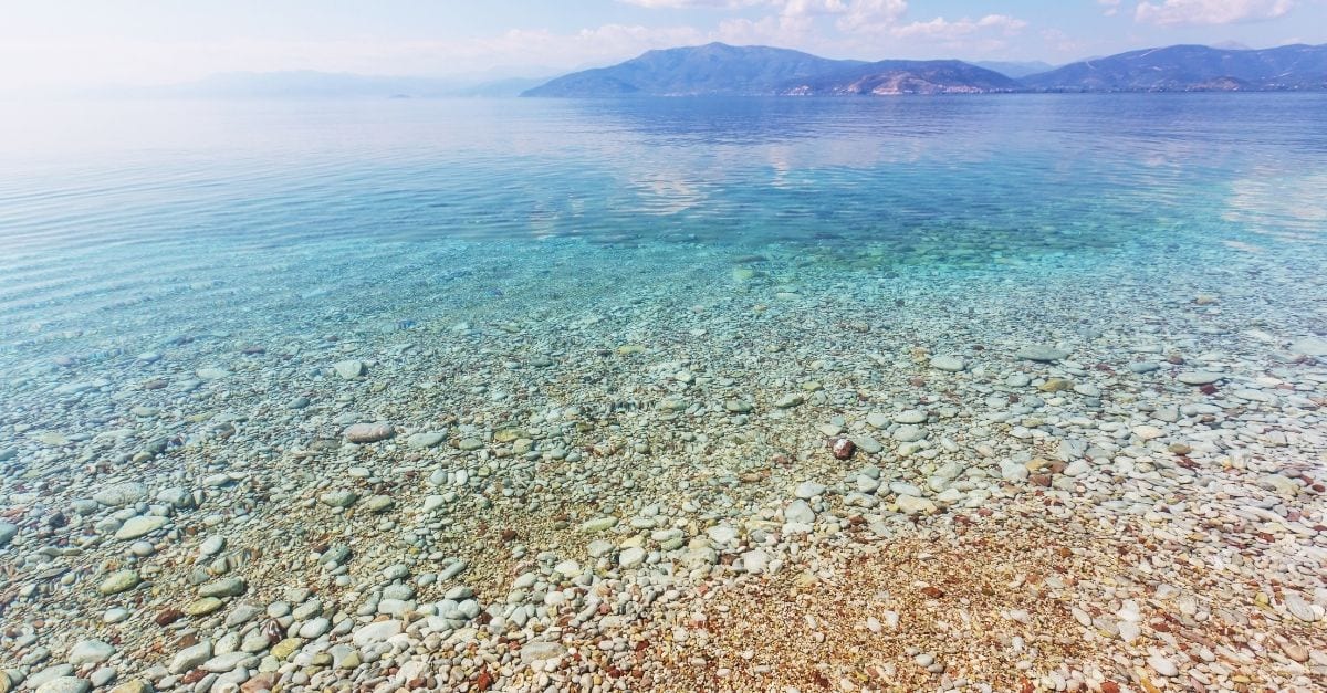 A trasparent blue-green ocean on a pebbly beach.