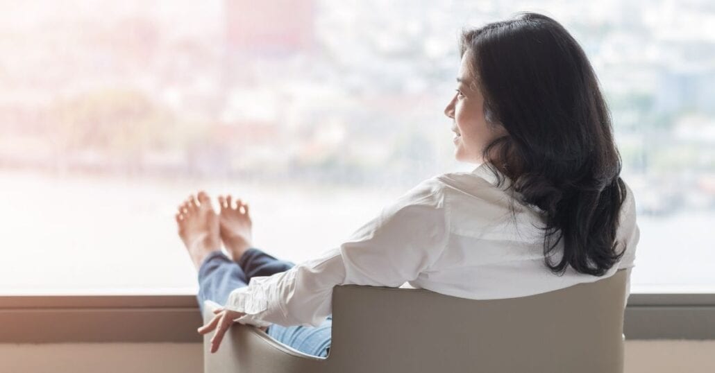 A woman sitting on a chair with her feet on a large windor. 