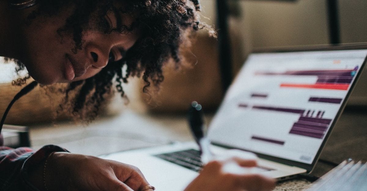 Young woman writing on a paper while studying in front of her laptop.