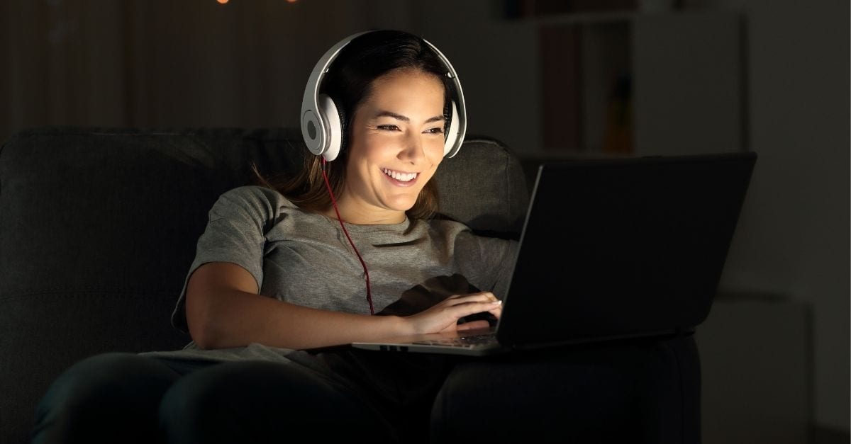 Woman smiling while watching a movie at nigh on her laptop.