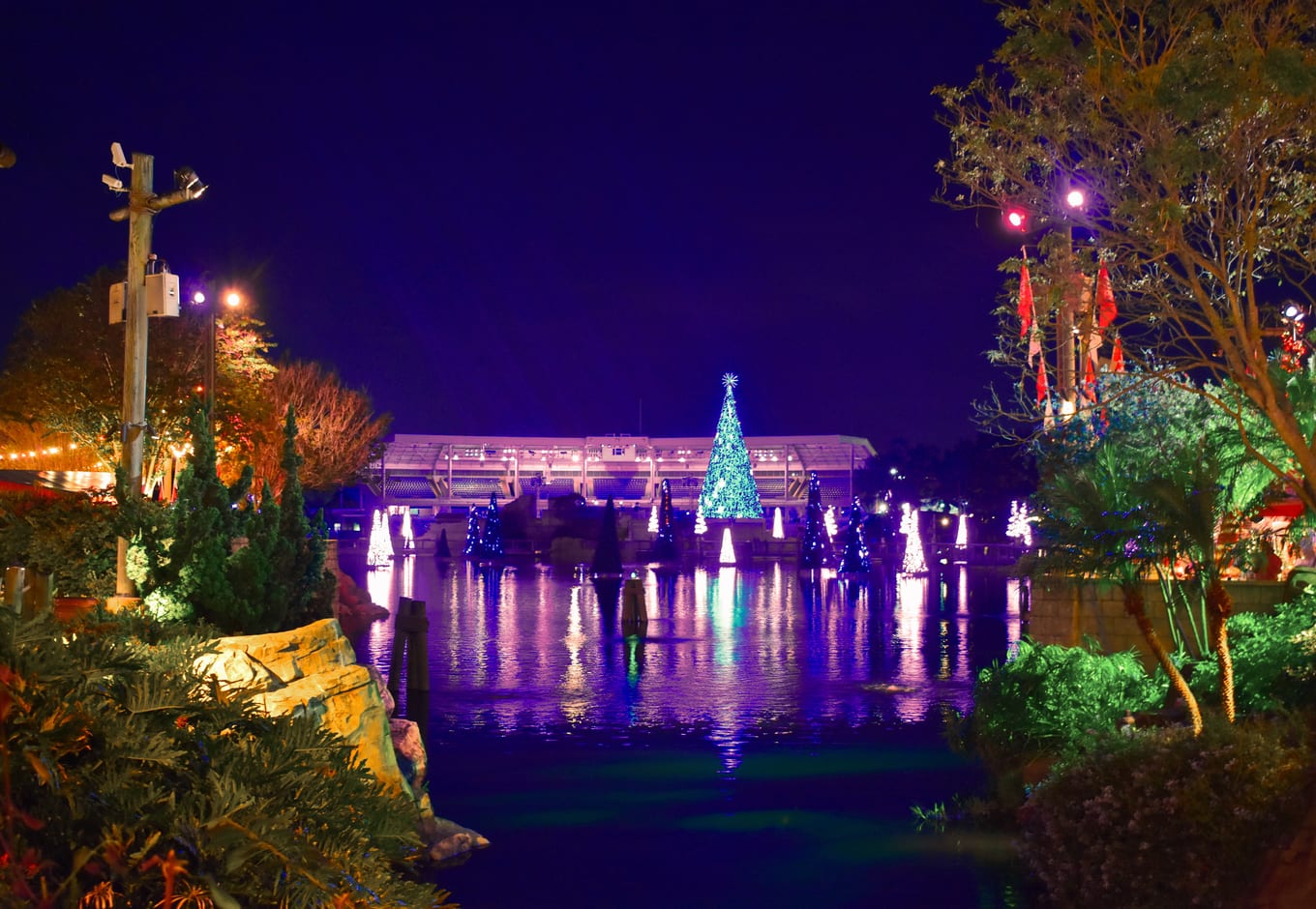 Amn illuminated landscape with rocks, trees, lake, a Christmas Tree and a colorful stadium on the International Drive area.
