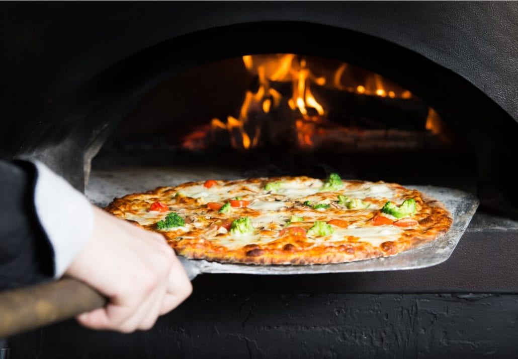 Hot pizza is removing from hot stove where it was baked. Cook using special shovel to removing them. This restaurant have special wood-fired oven.