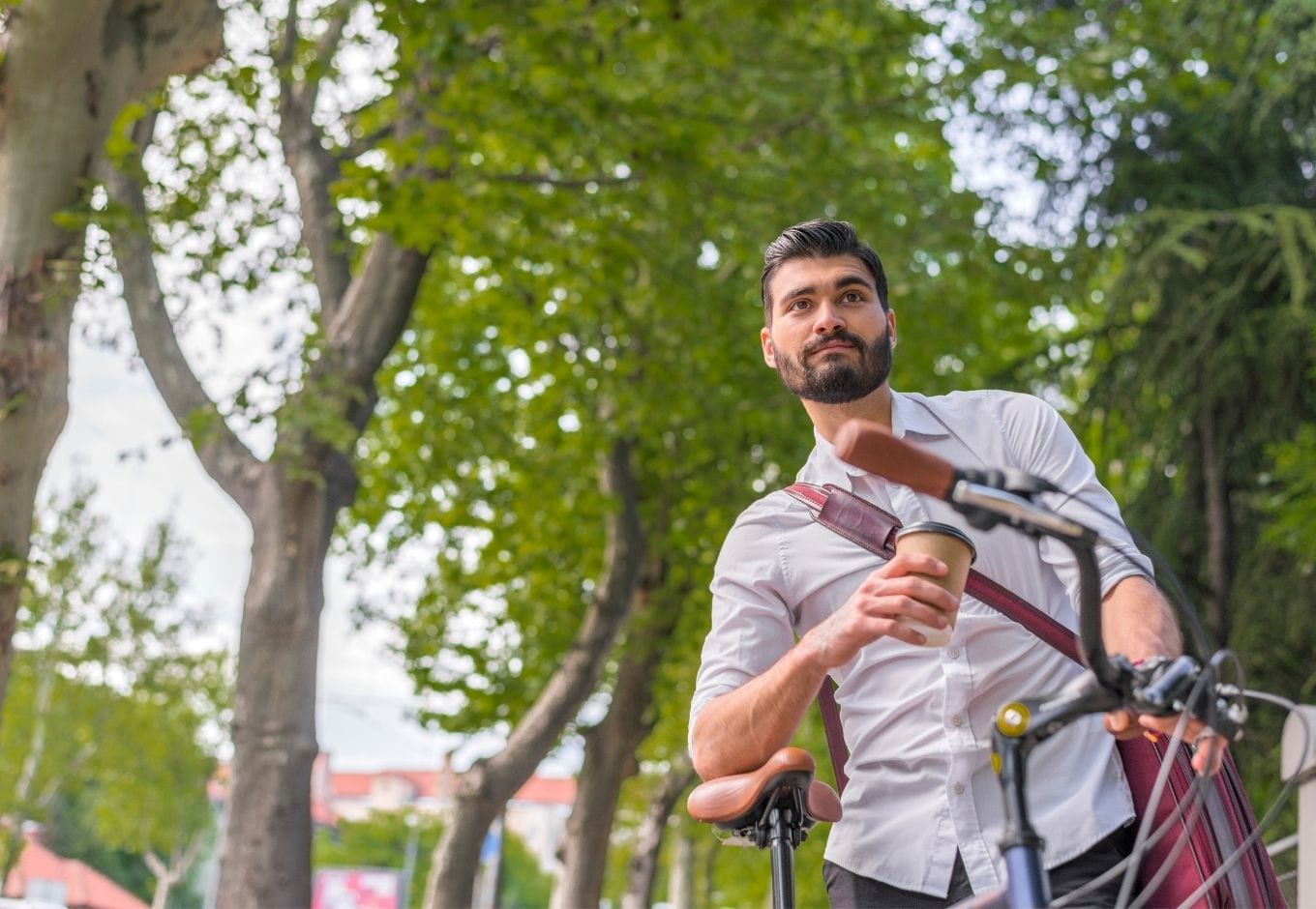 Man standing with his bicycle while holding a cup of coffee to go.