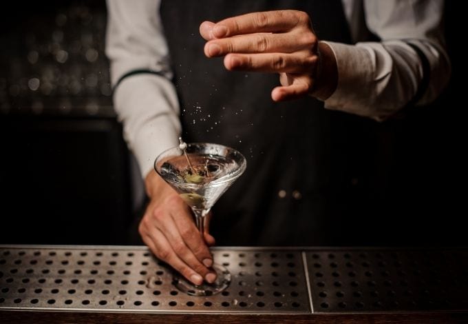 A mixologist seasoning a Martini with a pinch of salt.