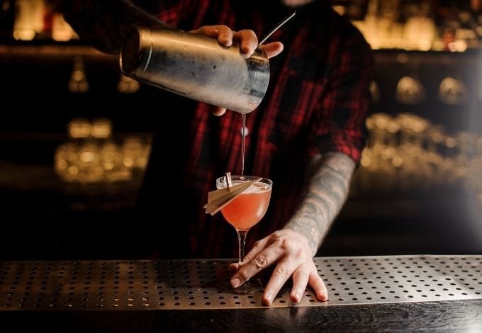 A bartender pouring a drink on a glass.