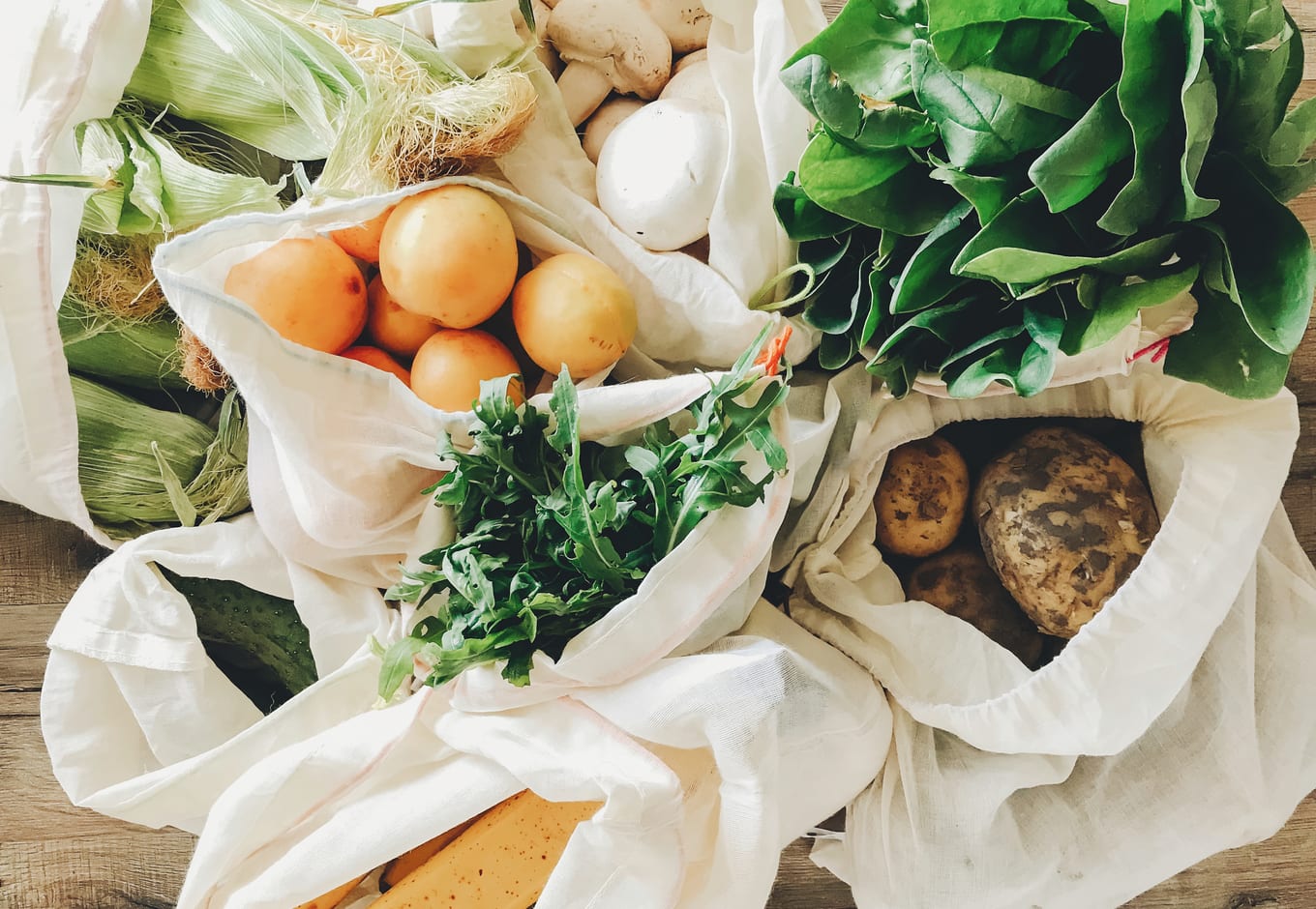 Organic vegetables (corn, tomatoes, potatoes, mushrooms), inside cotton bags.