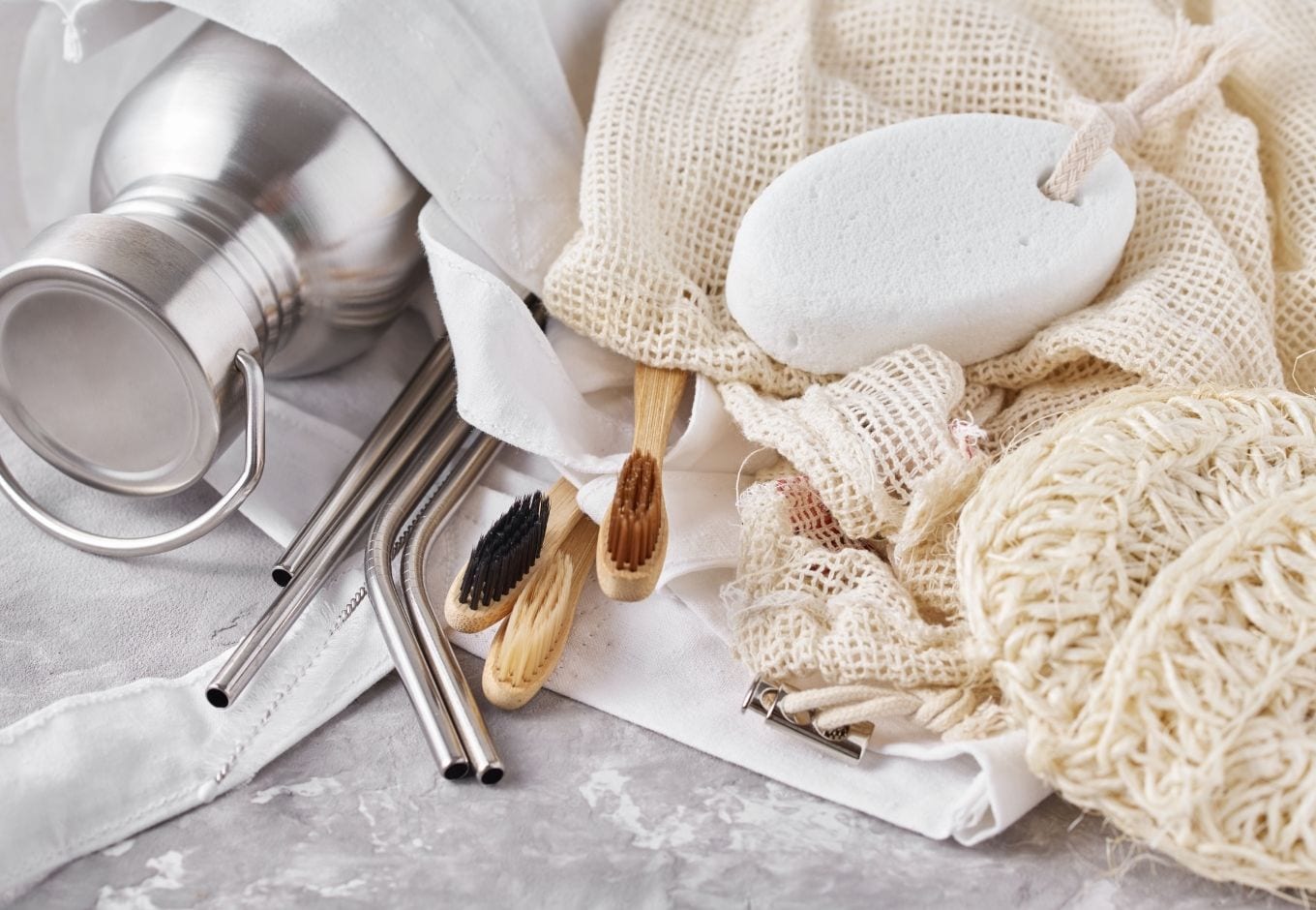 A set of reusable items: a water bottle, tooth brushes, straws and a sponge.