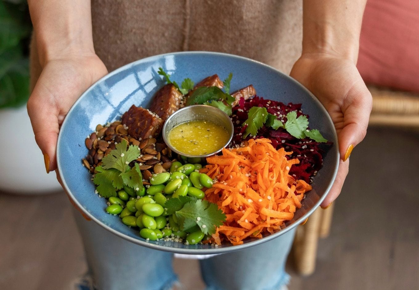 Woman holding a bowl with vegetables such as carrots, green beans and cilantro.