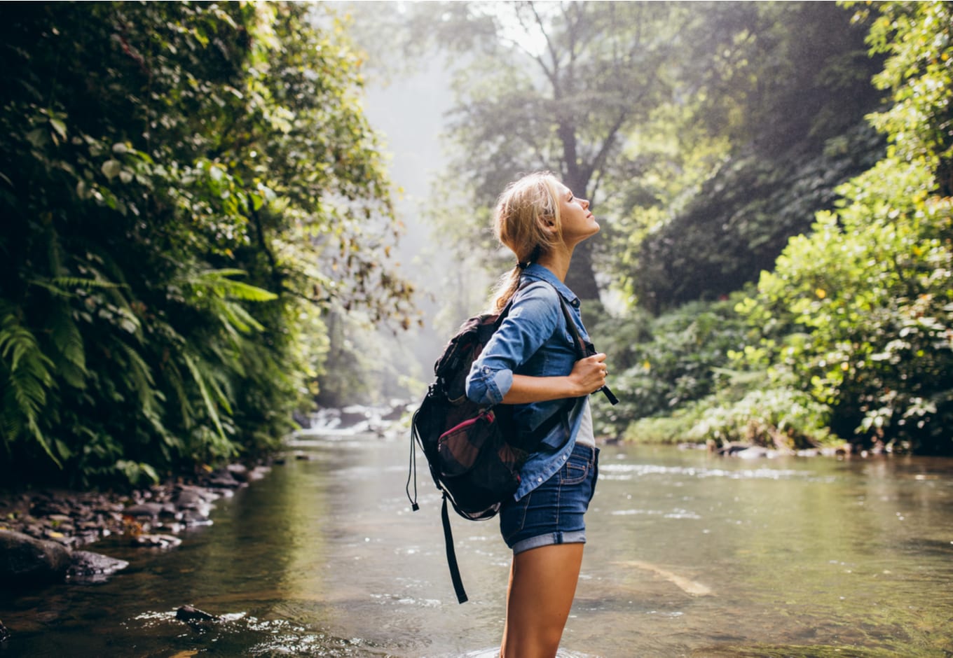 A young woman by a river surrounded by a green forest.