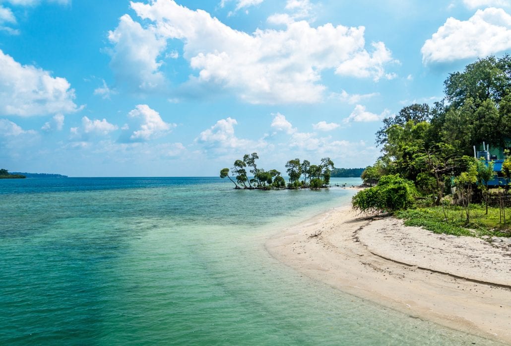 A white sand beach with transparent blue-green water in the Andaman and Nicobar Islands, India.