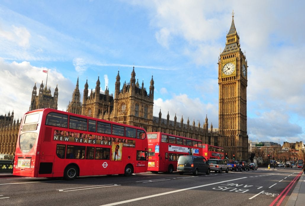 Three double-deck red buses in front of the Big Ben and the Westminster Palace in London.