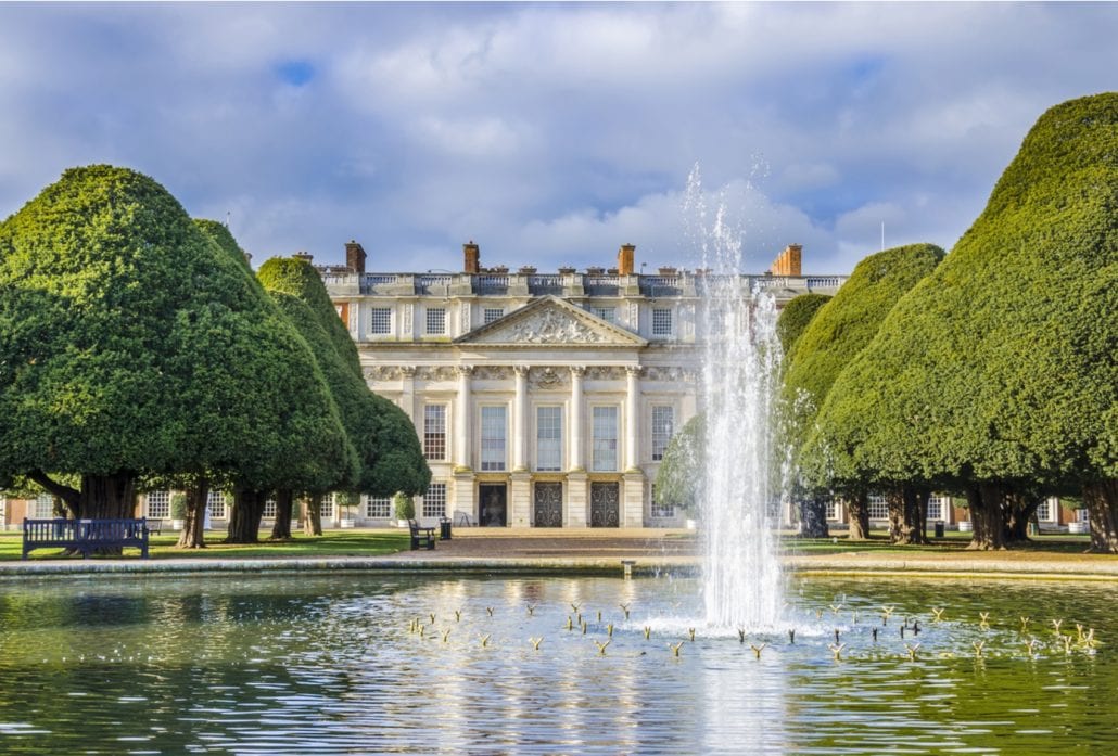 A water fountain and ornate trees in front ot the marvelous Hampton Court Palace, in London.