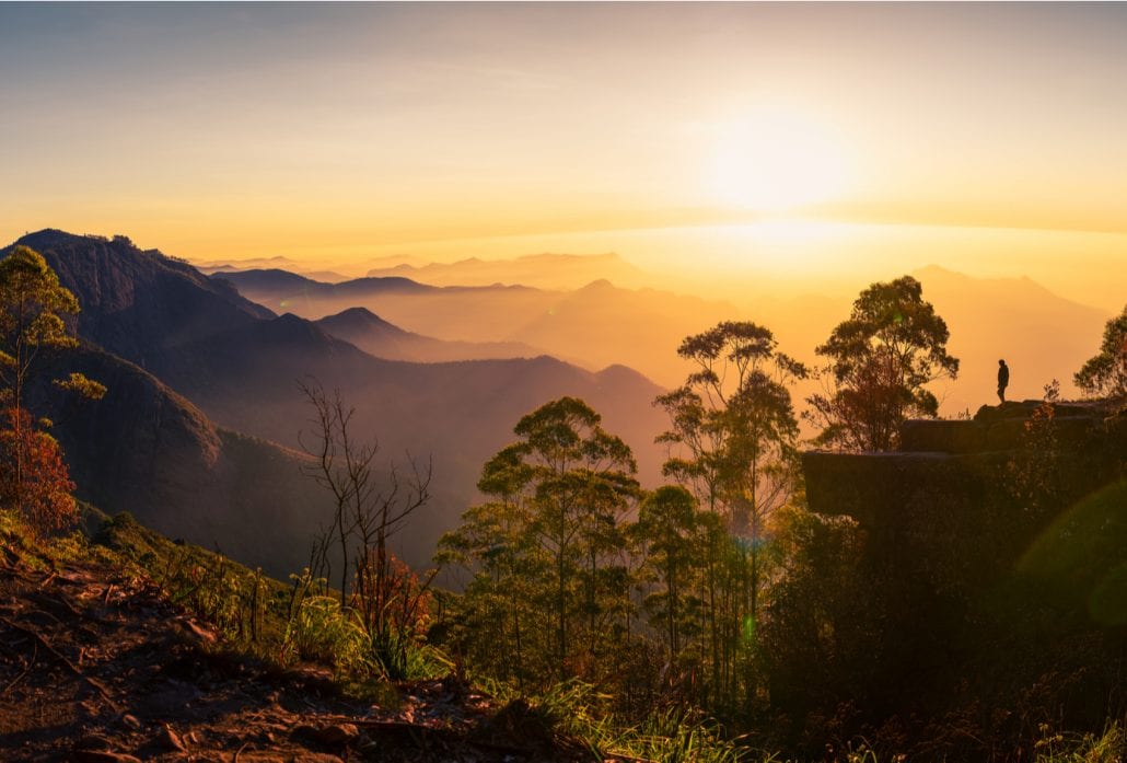 Silhouette of a woman watching the sunrise at the dolphin's nose in Kodaikanal, India.