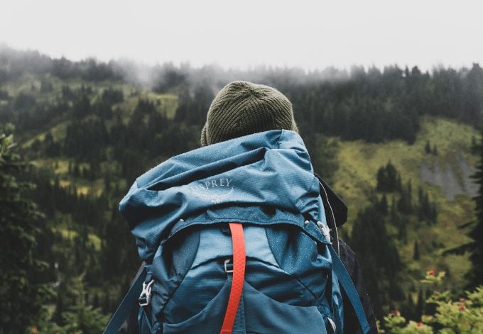 A young backpacker man looking at a forest on a cloudy day.