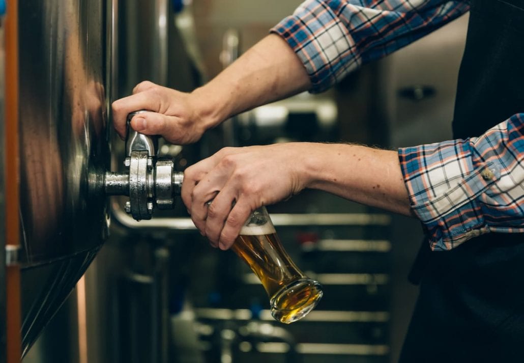 Brewer filling beer in glass from tank at brewery. Family business concept.