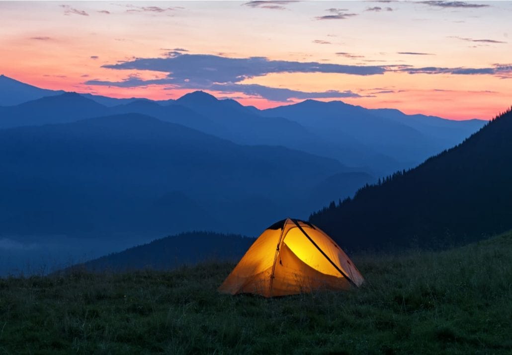 Bright orange tent in mountains under dramatic evening sky. Red sunset and mountains in the background. Summer landscape. 