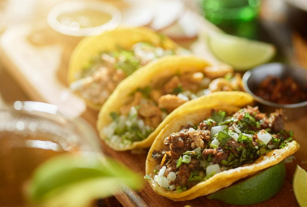 Three Mexican tacos on top of a wooden board.