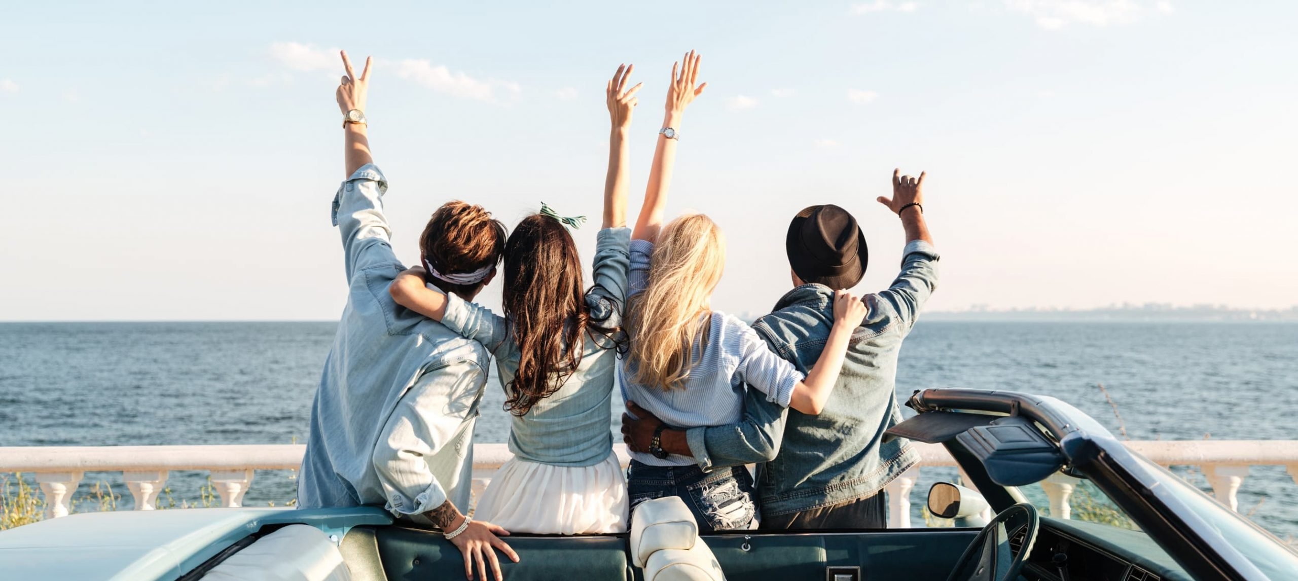 A group of four friends, two girls and two boys, on a car, celebrating during a weekend trip together.