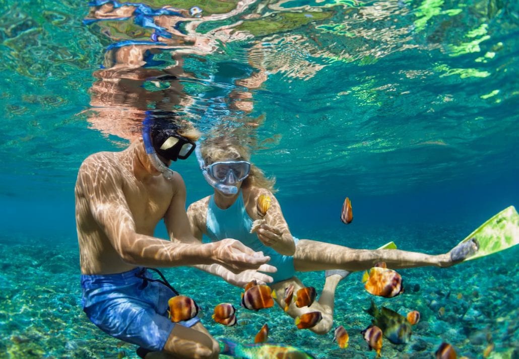 Young couple in snorkeling mask hold hand, dive underwater with fishes in coral reef sea pool.