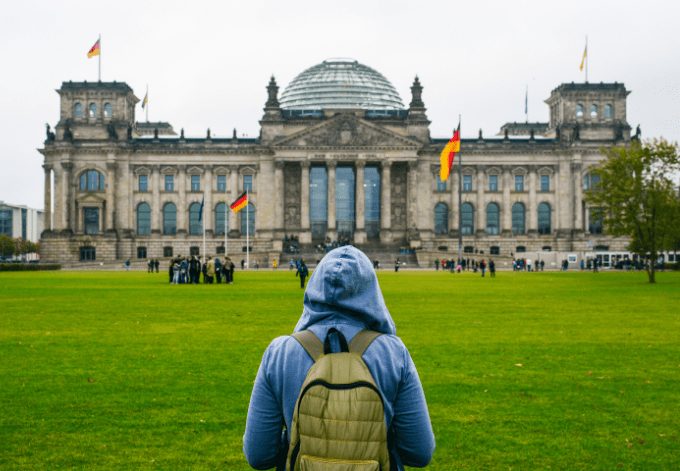 Young woman with backpack looking at the Bundestag building in Berlin. Erasmus student, studying abroad and tourist concept.