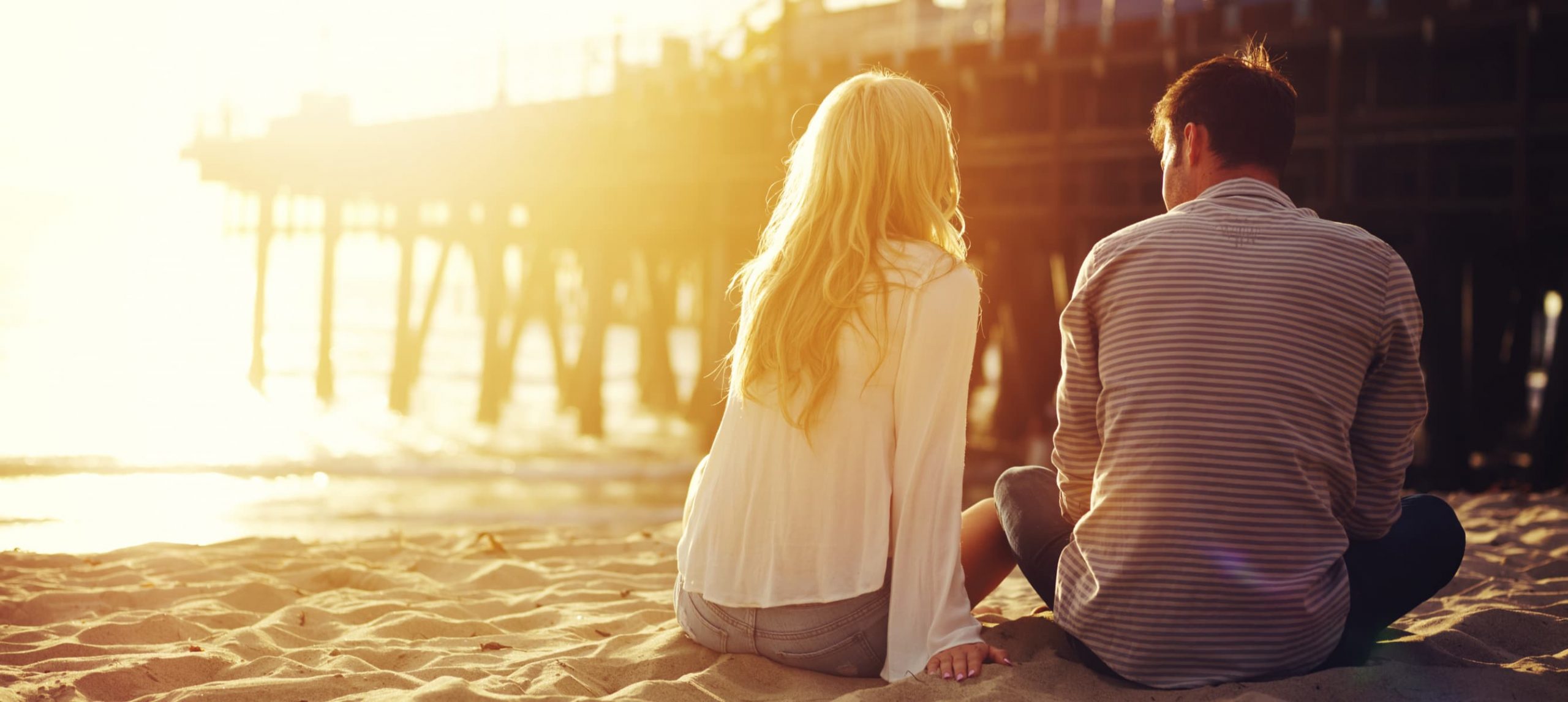 Romantic couple sitting together by the beach with sunset