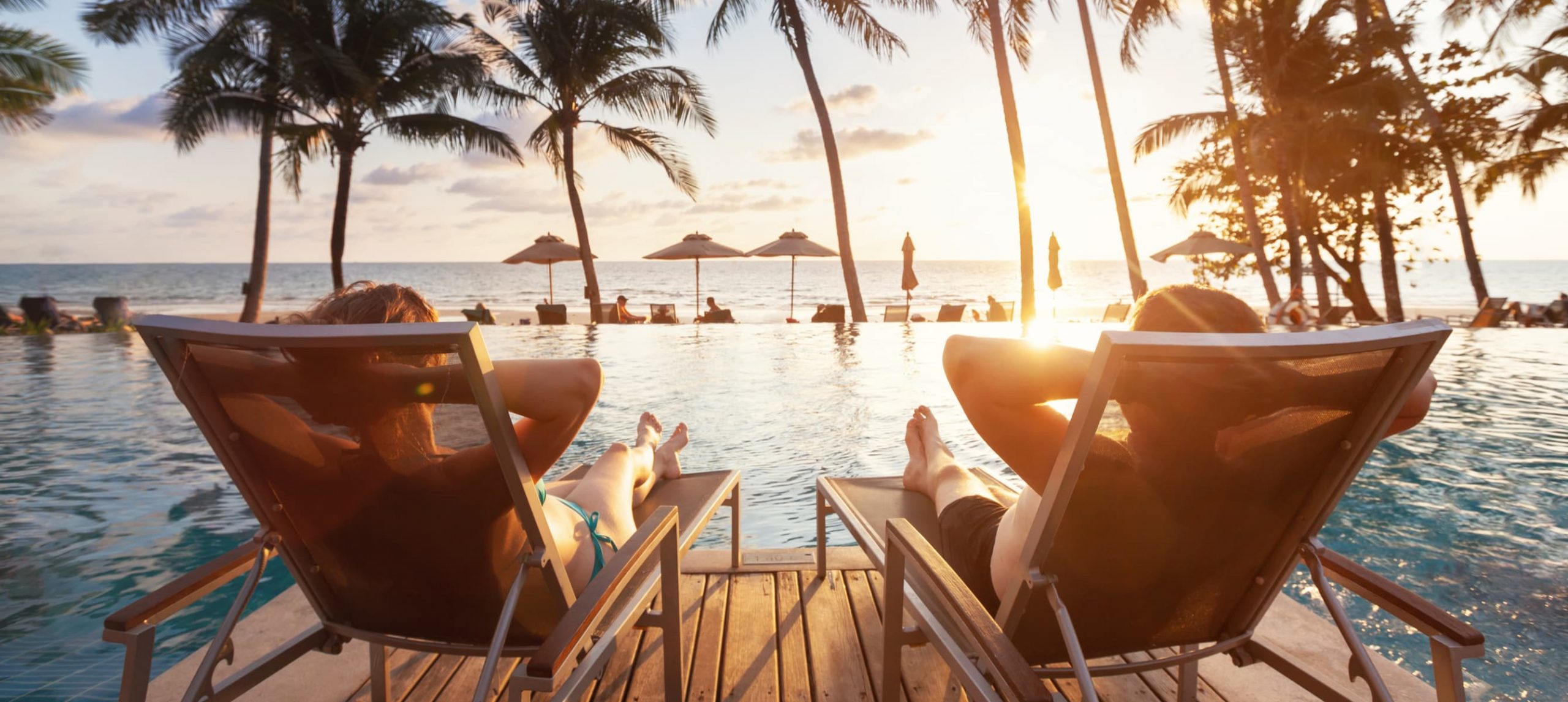 Couple having relaxing by the pool at a luxurious resort at sunset time.