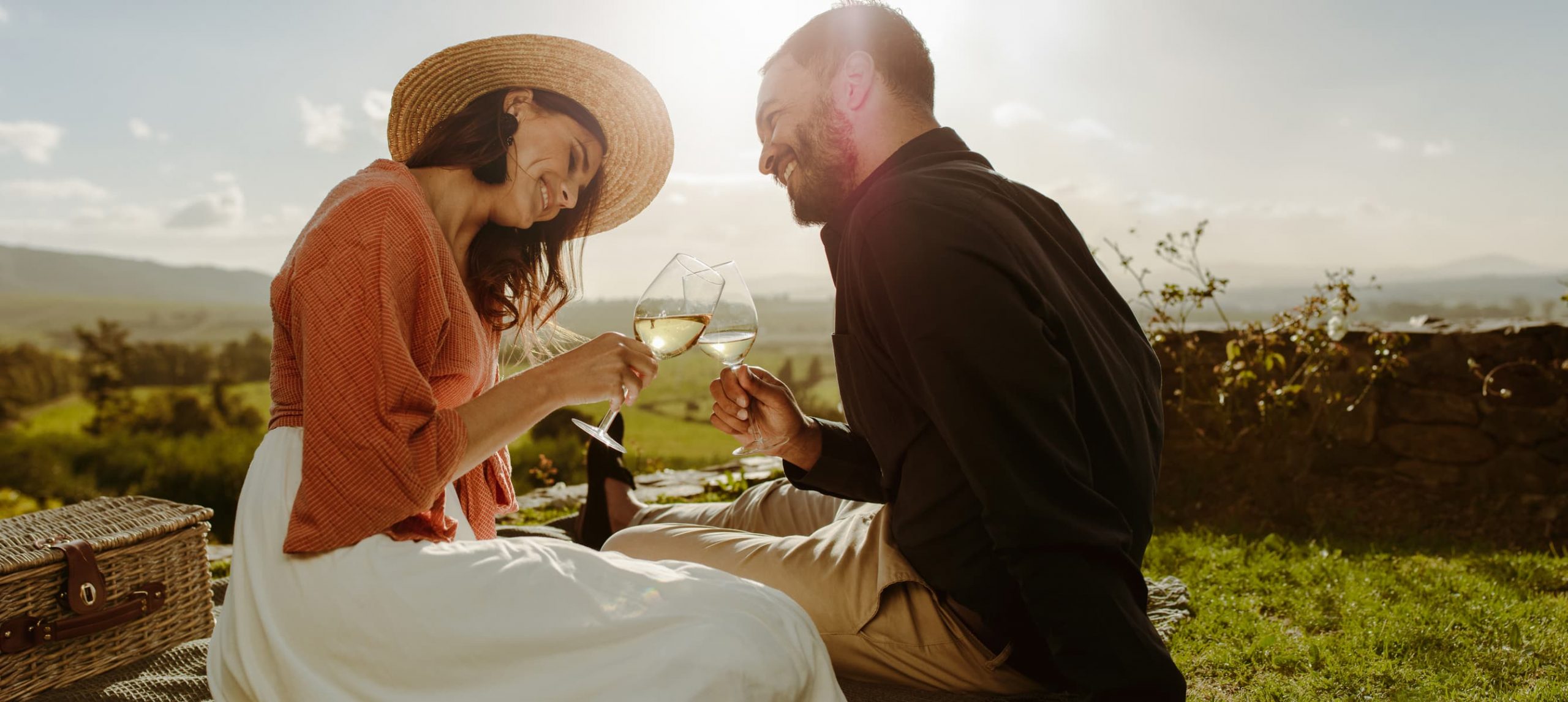 A smiling couple toasting at a vineyard during a sunset picnic.