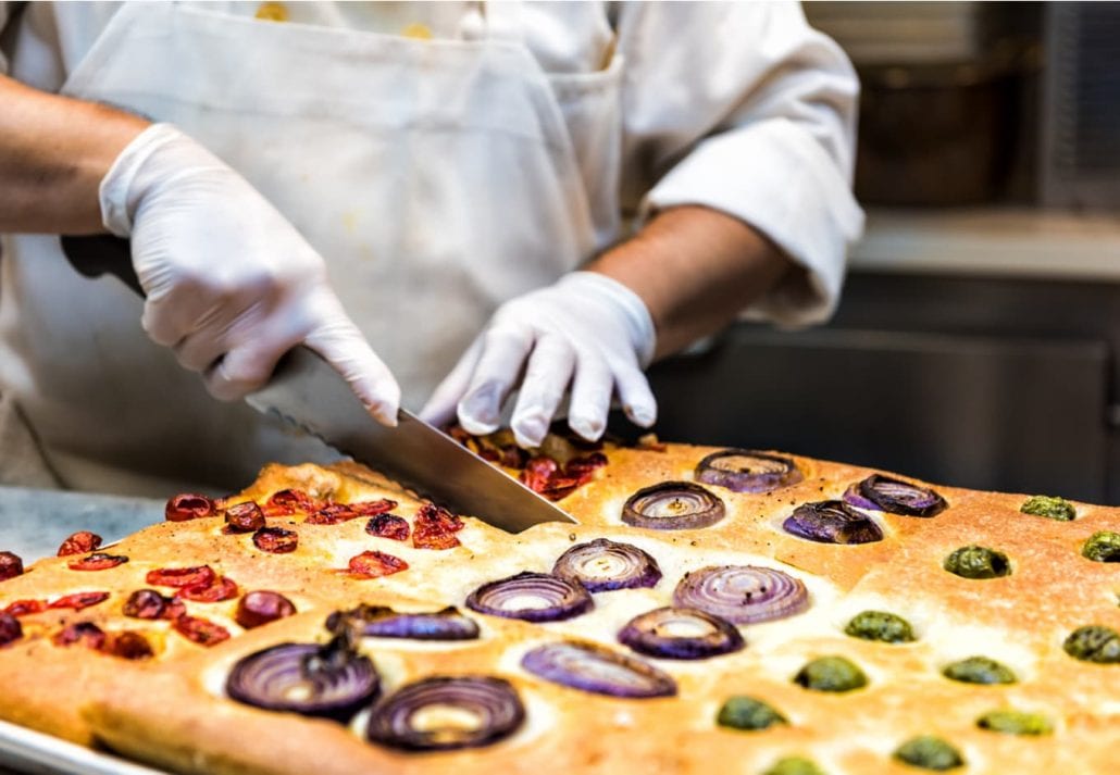 A person cutting a foccacia bread at a restaurant.