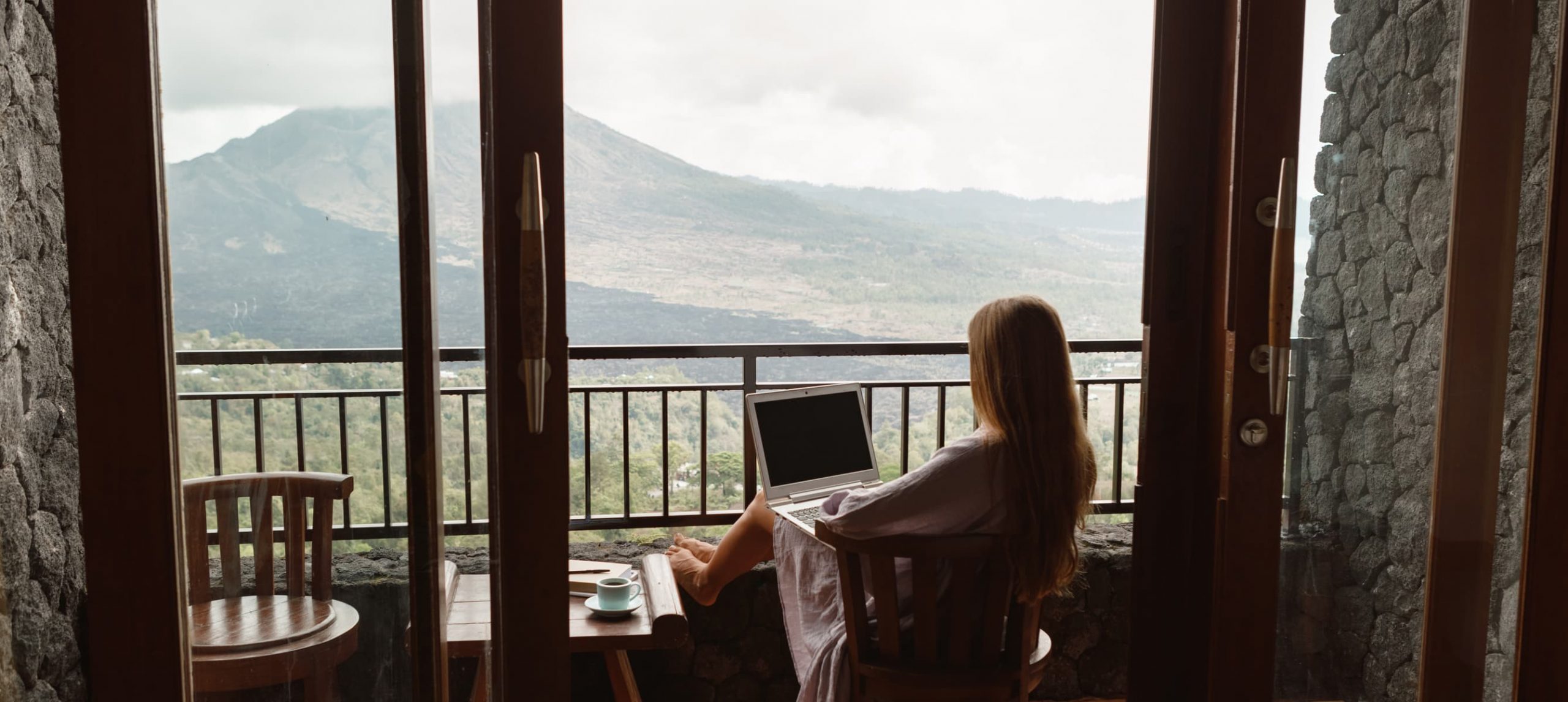 Remote girl working on her laptop on a hotel deck overlooking mountains.
