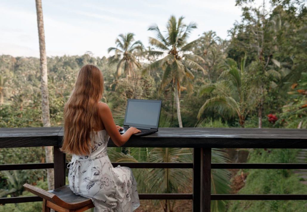 Remote work in tropic country. Woman working with laptop wjile sit in cafe with jungle view, coconut palms around