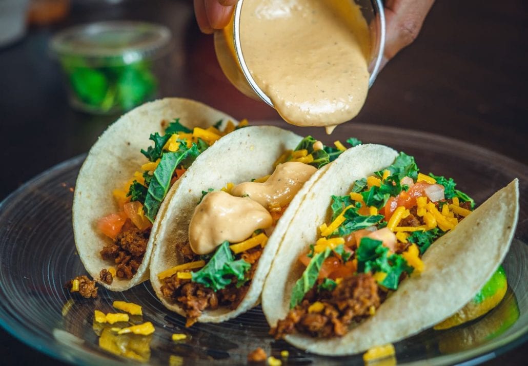 A person pouring a creamy sauce on a taco.