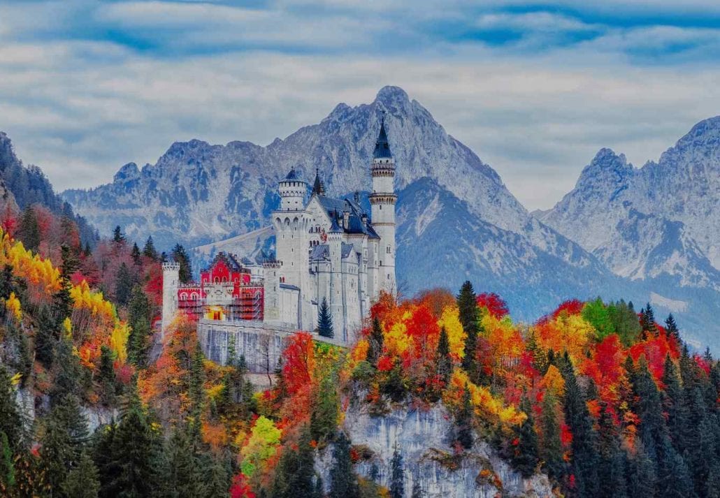 The neuschwanstein castle surrounded by orange, yellow and red fall foliage, in Germany.