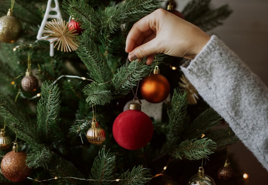 Woman decorating christmas tree with red bauble closeup.