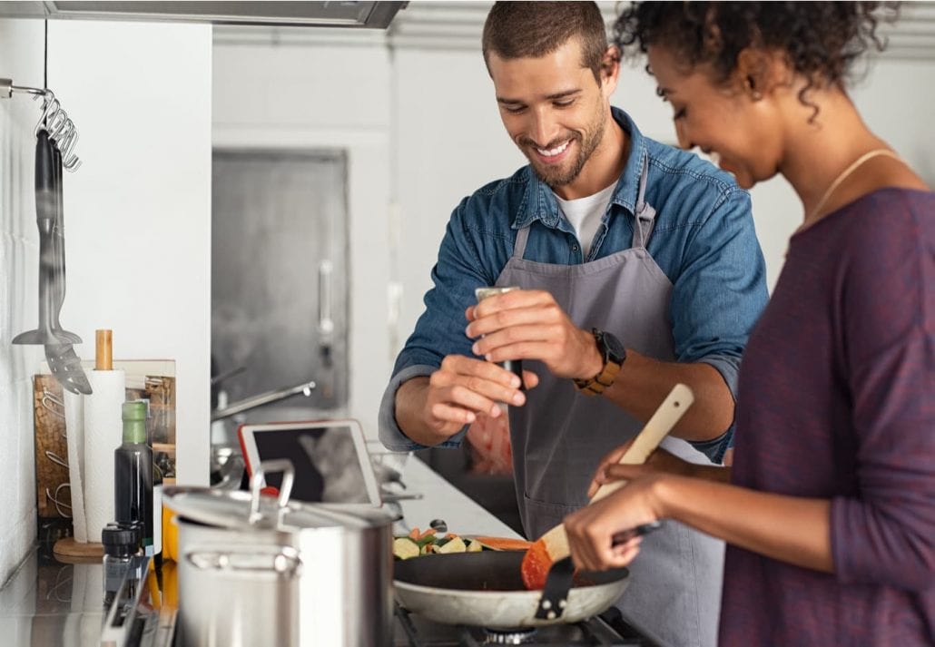 Young man cooking with girlfriend and adding spice to the sauce.