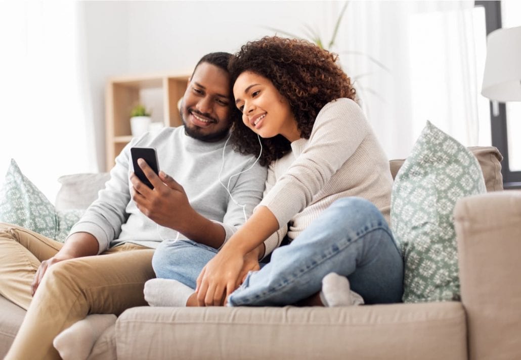 Happy couple with smartphone and earphones at home