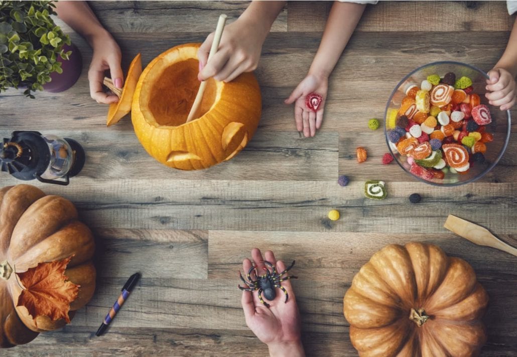 A mother, father and their daughter carving pumpkin on the table at home. Family getting ready for Halloween.